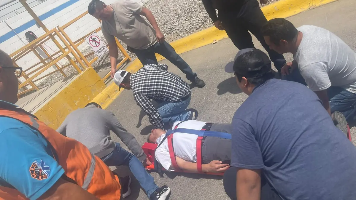 Brigadistas atienden a un compañero inmovilizado en una camilla rígida sobre el pavimento del patio de una planta, junto a un barandal amarillo