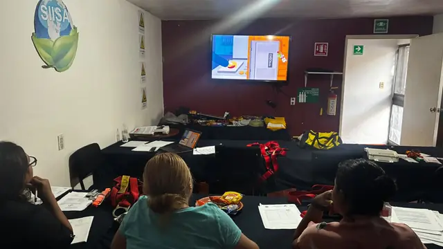 Participantes sentados en un aula de capacitación frente a una pantalla, con cascos y equipo de protección sobre las mesas