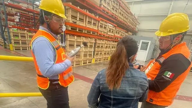 Safety supervisor in a high-visibility vest giving instructions to two workers on the plant floor