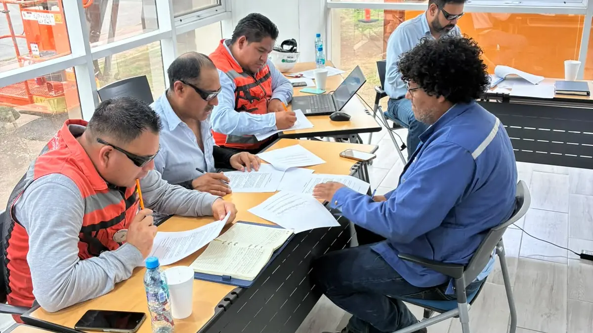 Dos supervisores con chaleco de seguridad revisan carpetas y formatos sobre un escritorio en la oficina de una planta