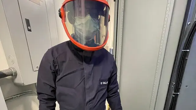 Técnico con traje de protección contra arco eléctrico y careta frente a un tablero