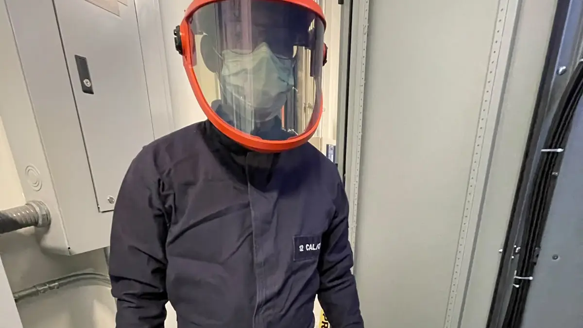 Técnico con traje de protección contra arco eléctrico y careta frente a un tablero
