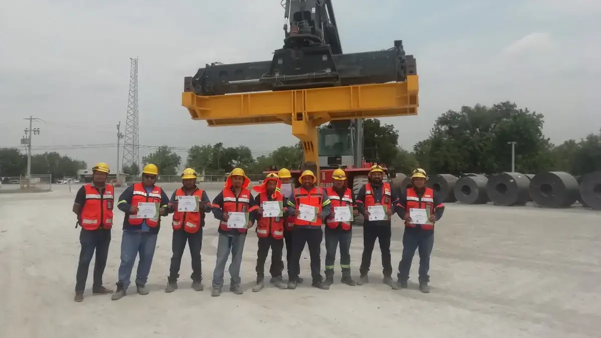 Yard crane lifting a shipping container while a training group stands in the foreground