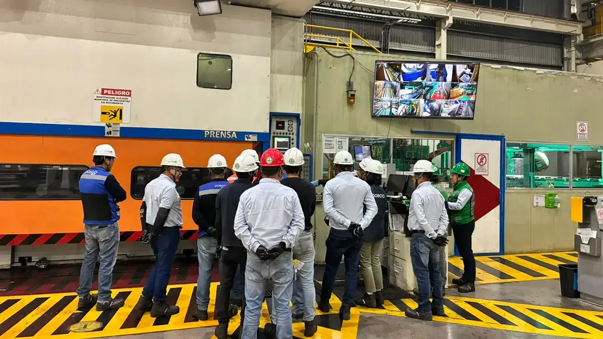 Workers in hard hats and safety vests at a safety briefing beside a press line