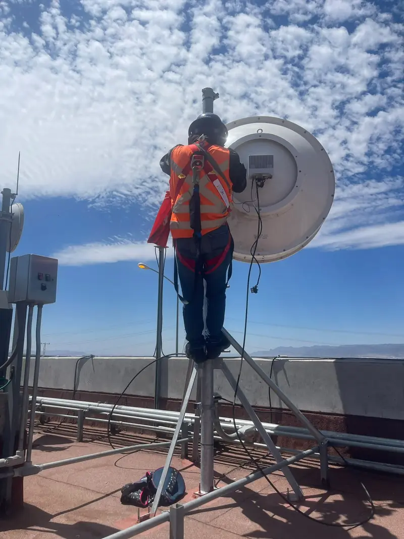 Trabajador con arnés sobre un mástil elevado haciendo mantenimiento en la azotea de una nave industrial