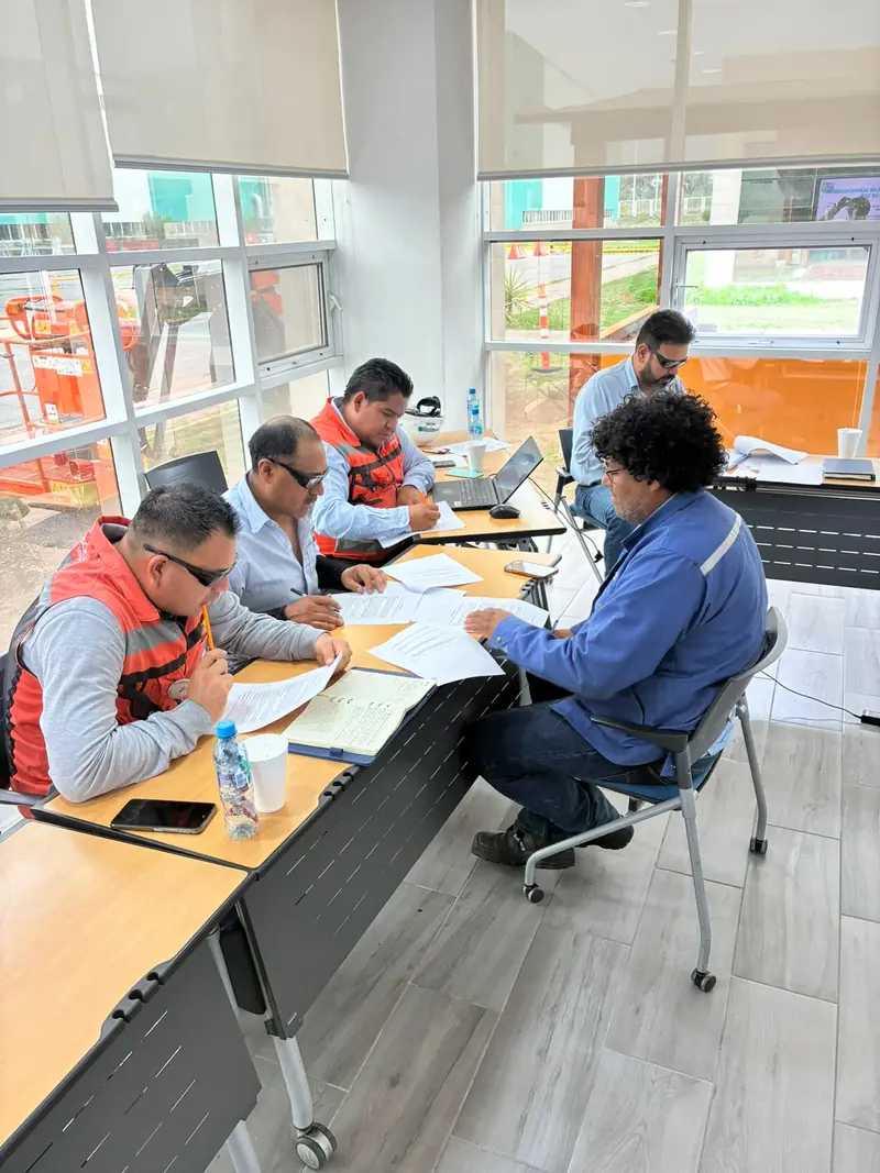 Participantes con chaleco responden por escrito en la sala de capacitación de una planta