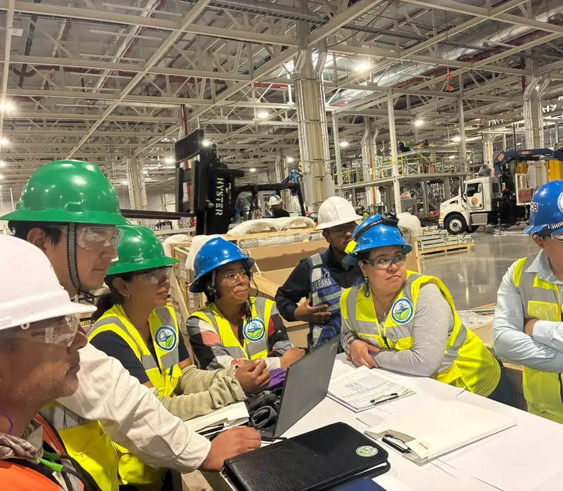 Equipo de SIISA con chalecos y cascos revisa documentos en una mesa de coordinación dentro de la nave en construcción