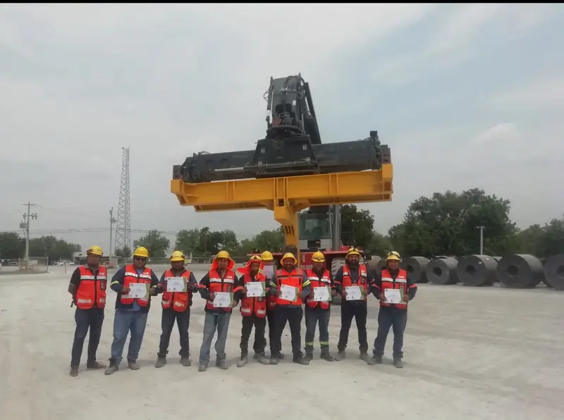Grupo de participantes con chaleco y casco al terminar una práctica de maniobras con grúa de patio