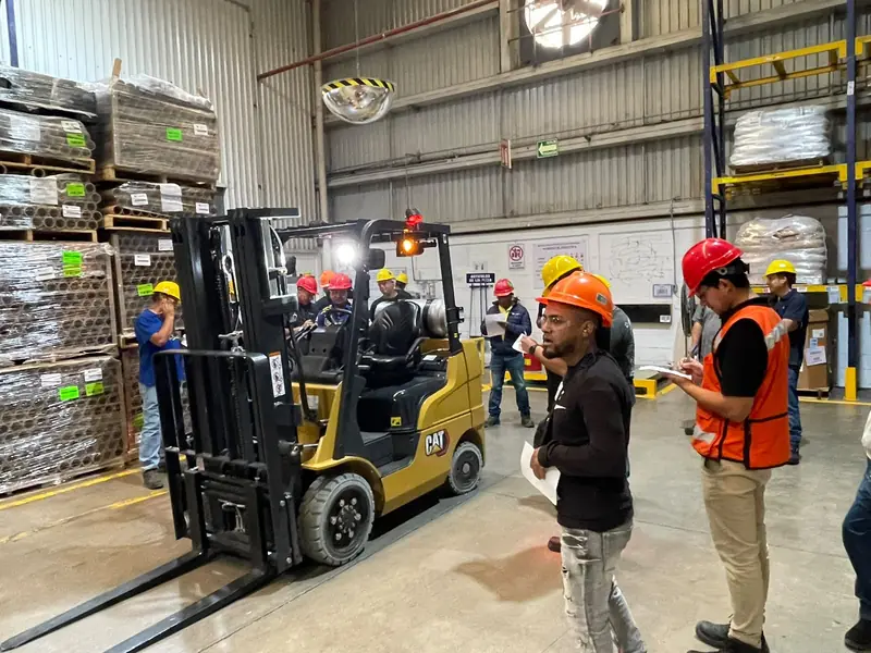 Instructor de SIISA explica la revisión previa de un montacargas a un grupo de operadores con casco y chaleco