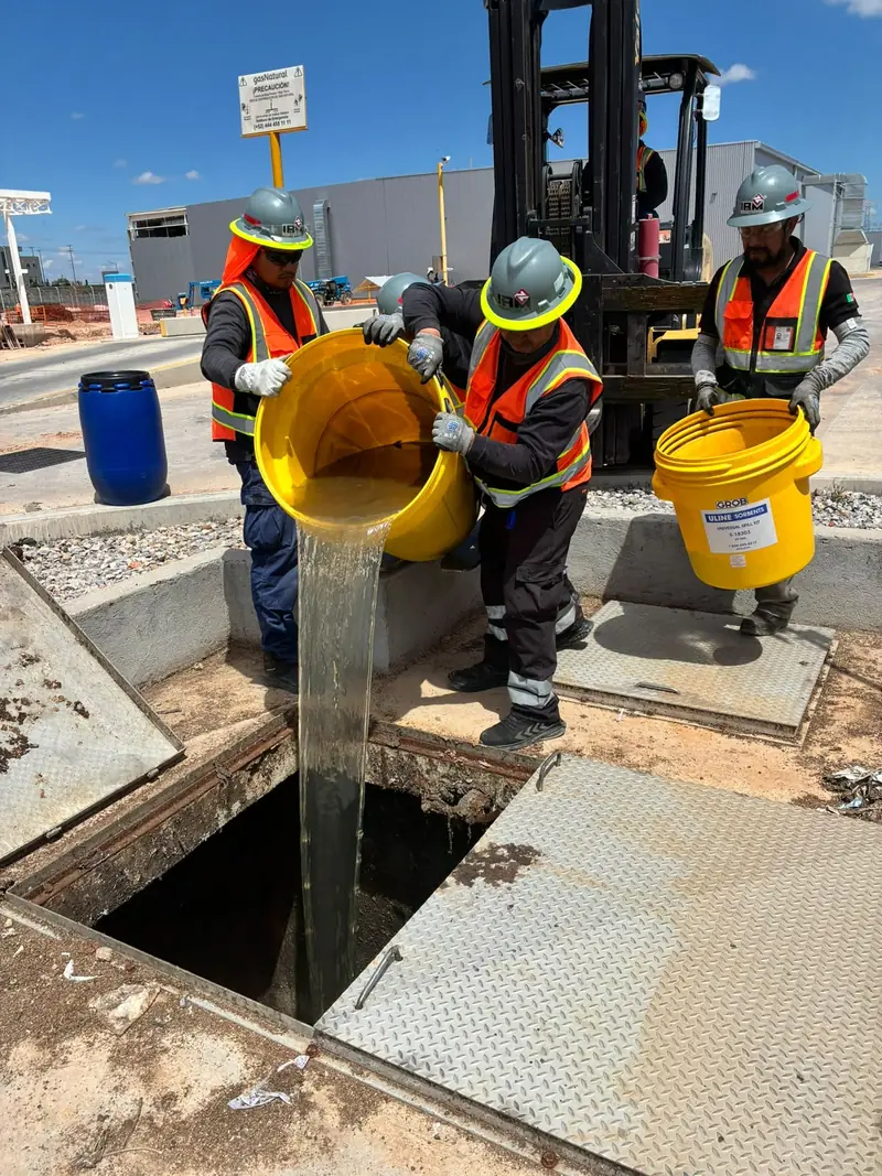 Trabajadores con equipo de protección vacían contenedores de líquido en un registro de piso