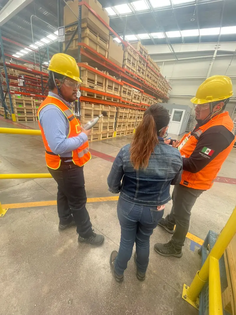 Supervisores de seguridad con chaleco revisan indicaciones con una trabajadora en el piso de planta